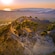The sun setting over a lush valley and mountain cliff with castle ruins